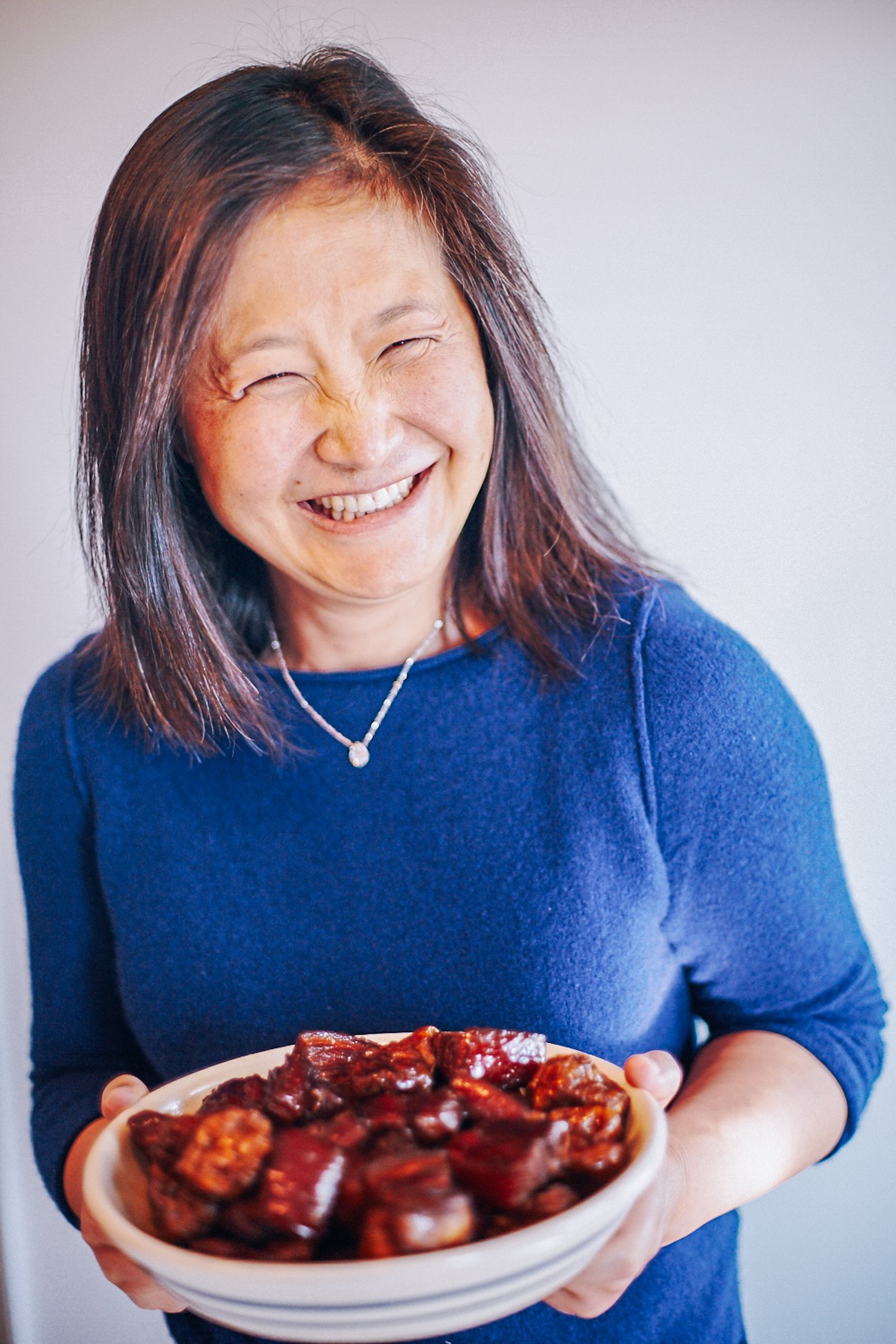 Judy holding plate of braised pork belly