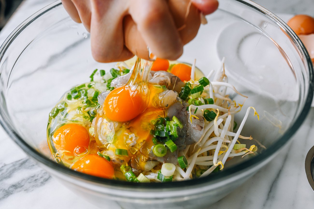 cracking eggs onto shrimp, bean sprouts, scallions